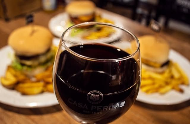 Taça de vinho tinto na mesa, com hambúrguer ao fundo